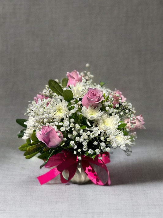 Arreglo chico con rosas rosadas, crisantemo blanco, gipsófila y follaje en una base de cerámica.