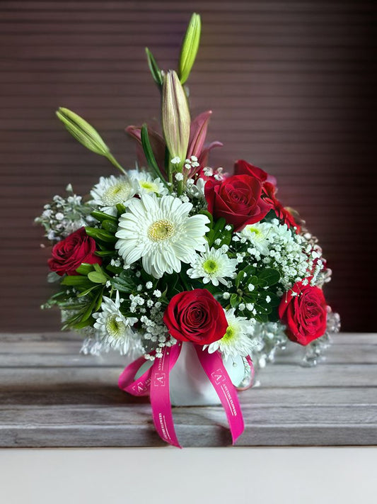 Arreglo mediano con rosas, lirios, gerberas, crisantemo, nube y follaje verde en base de cerámica..